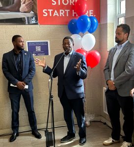 A man speaks behind a microphone while two men stand beside him