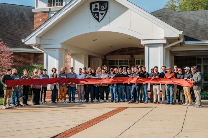 Ribbon cutting at Arsenal business Growth. A large group of people are standing in front of the building holding a red ribbon.
