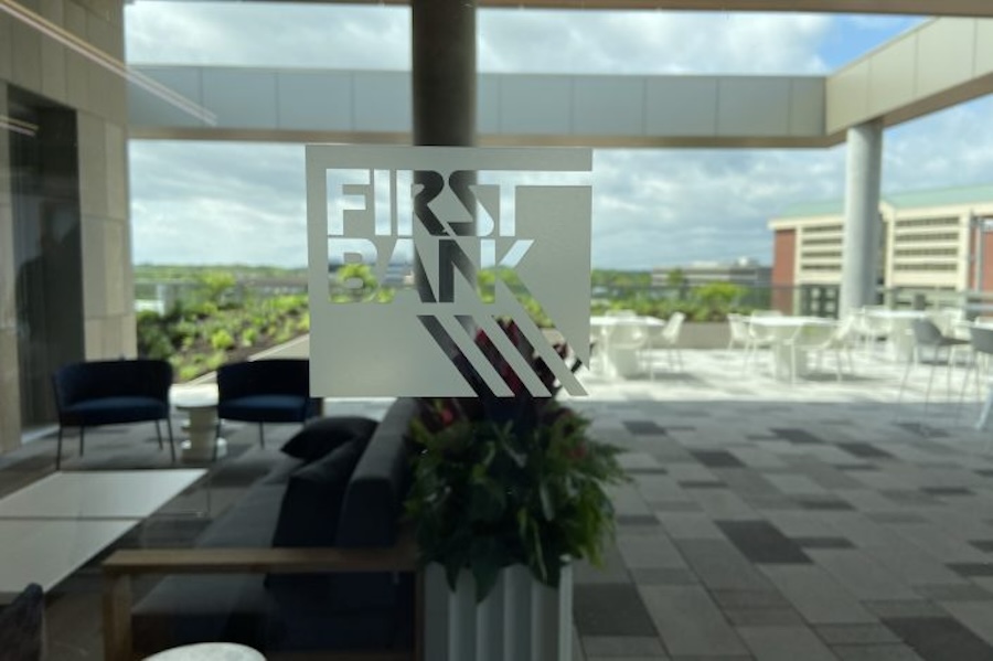 Window looking into an office space. The logo of First Bank is etched into the window glass