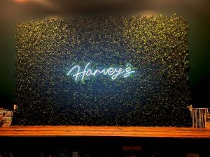 A neon sign saying Harveys is in front of a leaf background