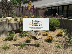A sign reads Brilliant Angels Academy - Welcome to the ribbon cutting of Brilliant Angels Academy 
