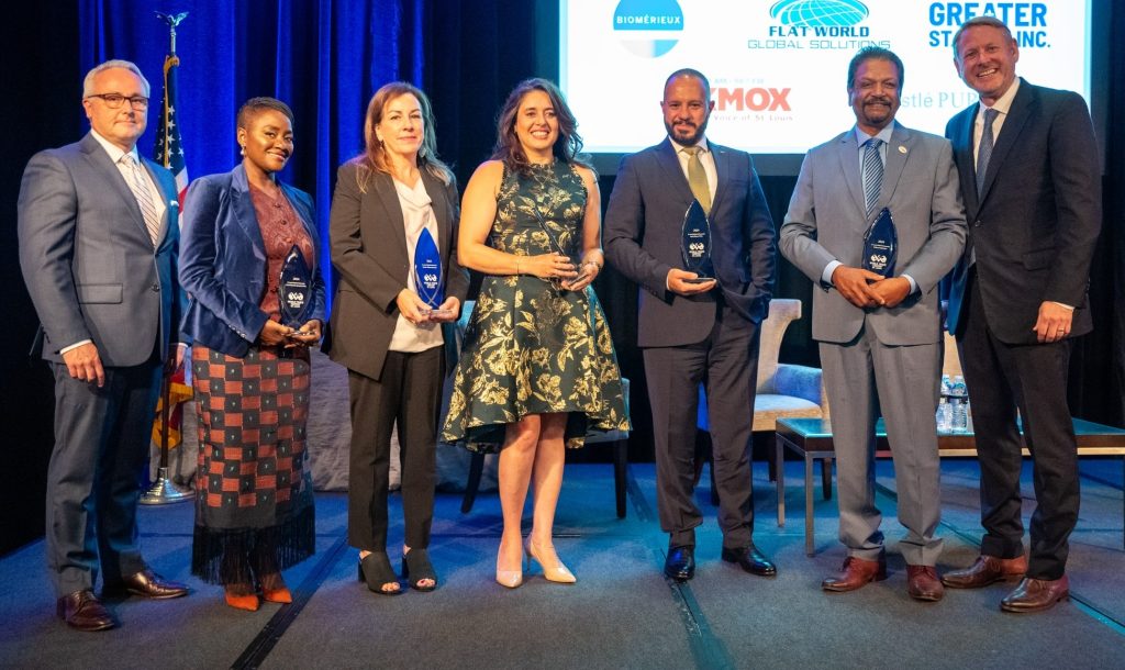 A group of people stand posed for a photo, 5 of them holding a glass award 