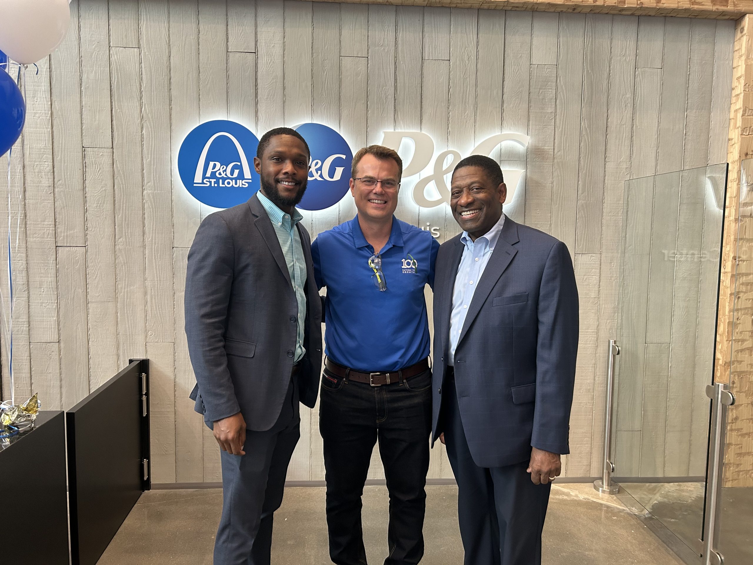 3 men stand posed in front of a P&G sign