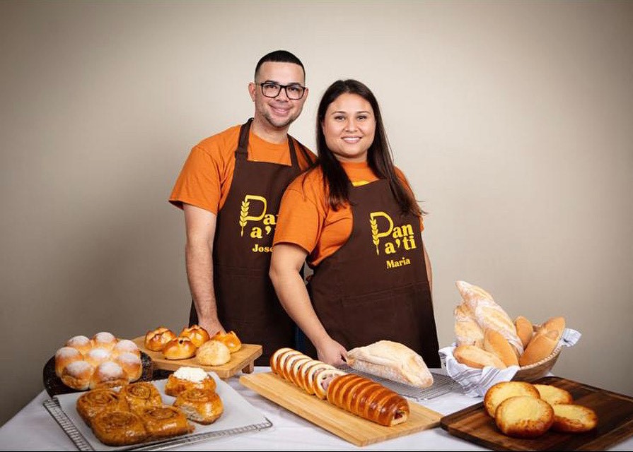 A man and woman stand in front of baked goods