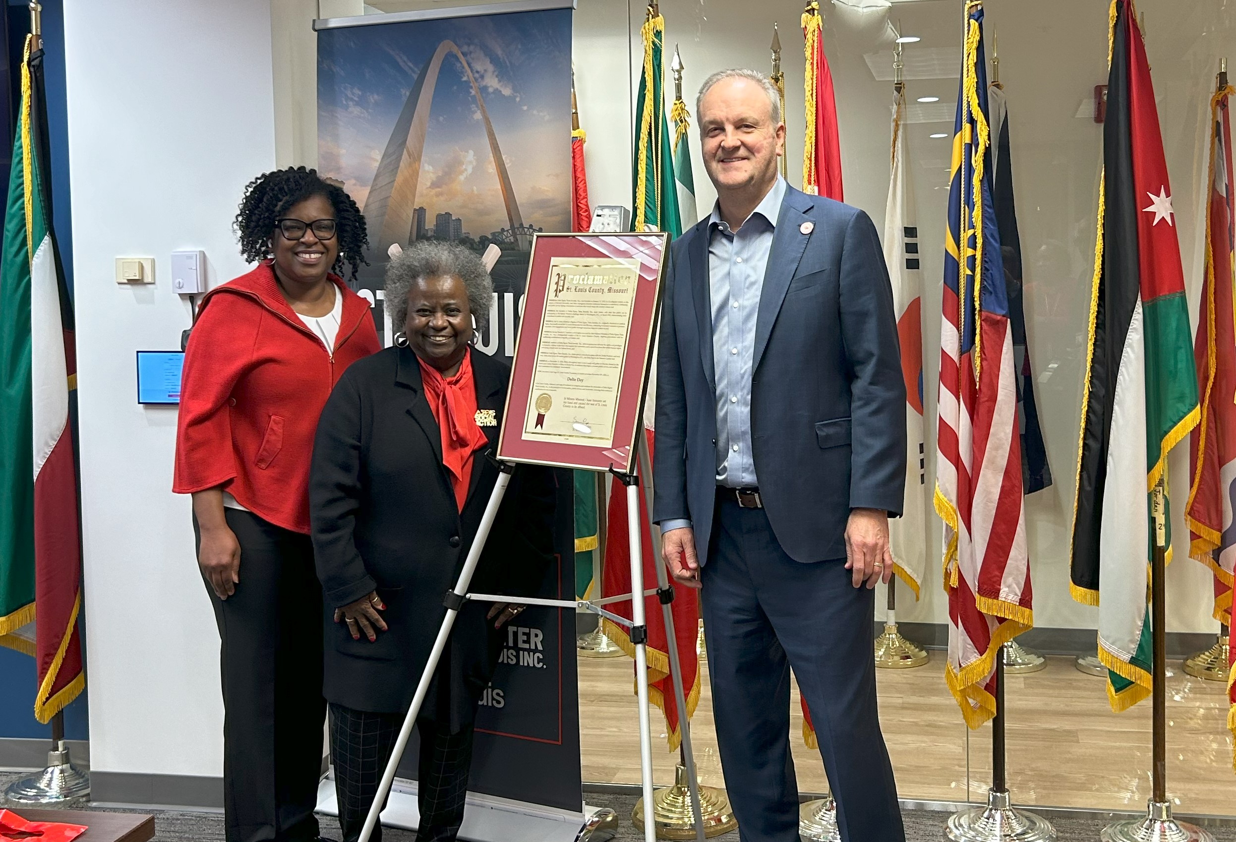 two women and a man stand in front of a sign on a pedestal