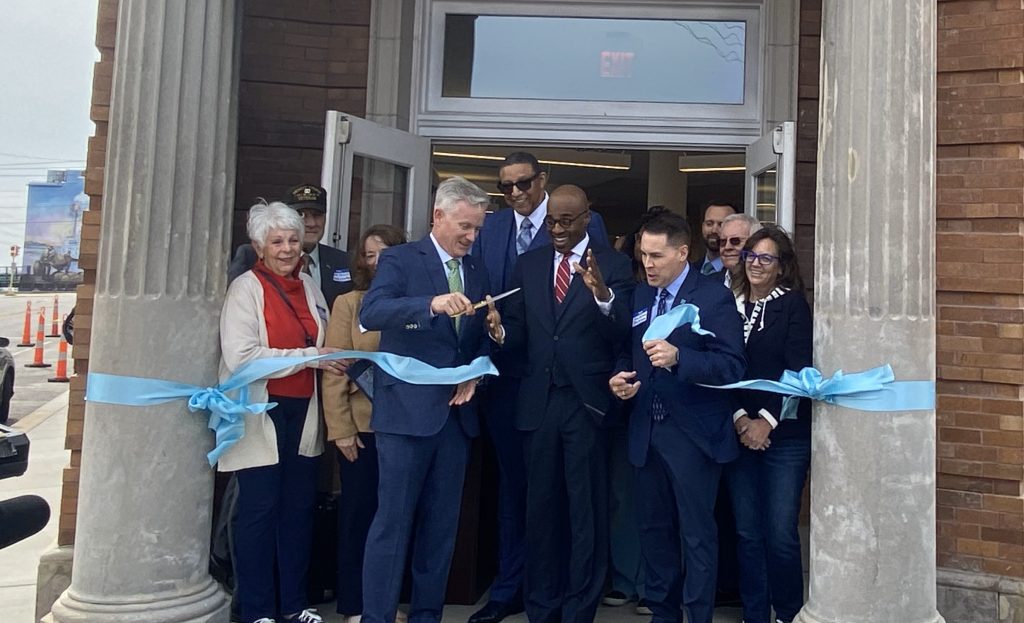 A group of people stand in front of a building and cut a large blue ribbon