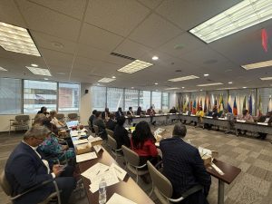 A large group sits at tables during a meeting