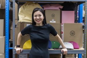 woman poses in front of shelf in warehouse with colorful bags