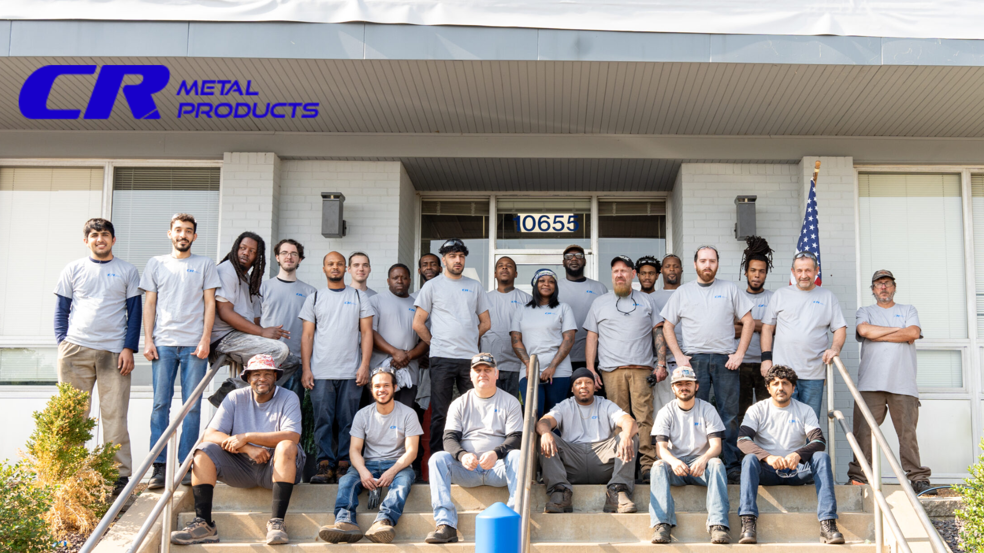 A group of people in matching grey shirts sit on steps outside