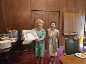 Two women stand together, one holds an arch