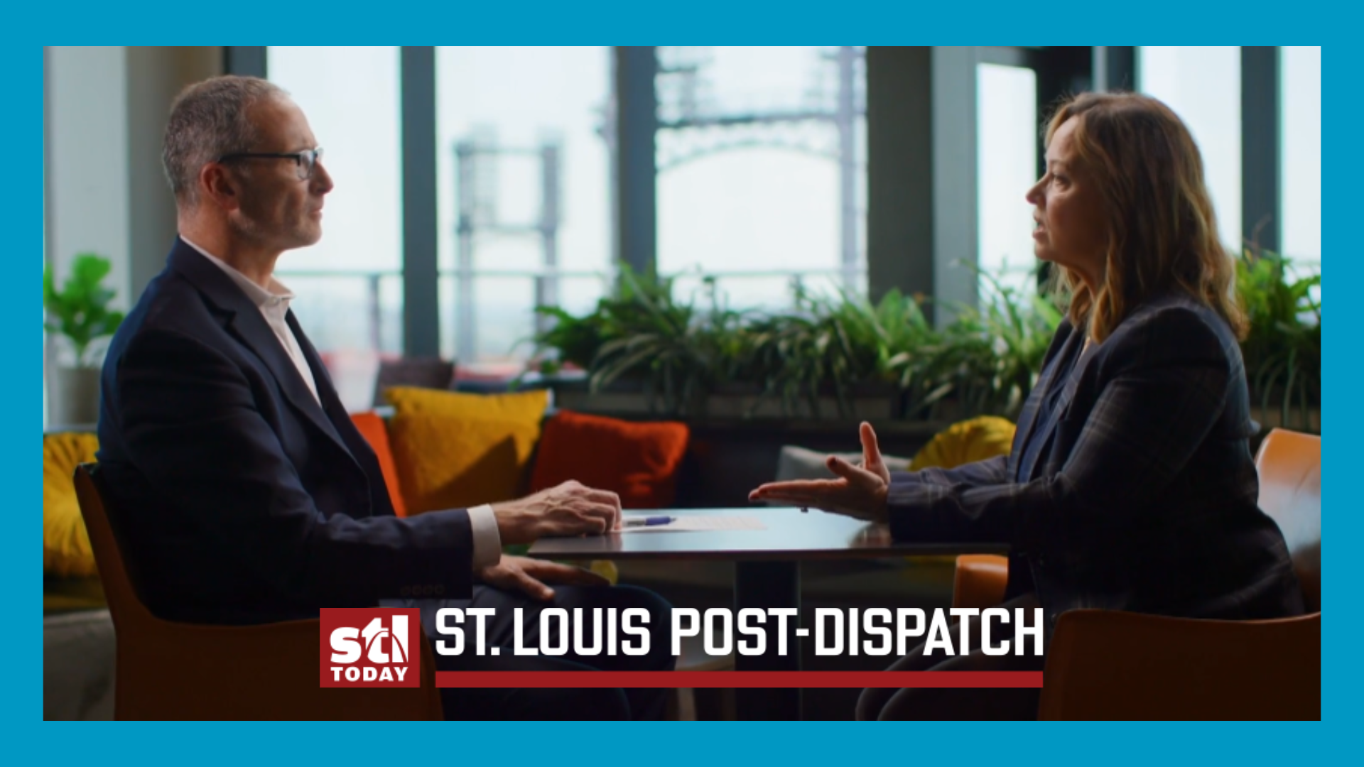 two people sit across a table. STL Post dispatch logo at bottom and everything is within a blue frame