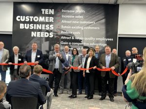 many people hold a red ribbon as it is cut with big scissors