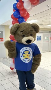 The build a bear mascot waves in front of a balloon arch