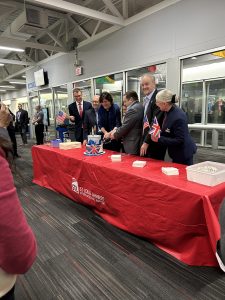 a group of people stand around a red table and cut cake