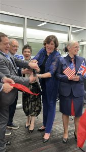 a group of people excitedly cut a large red ribbon inside an airport