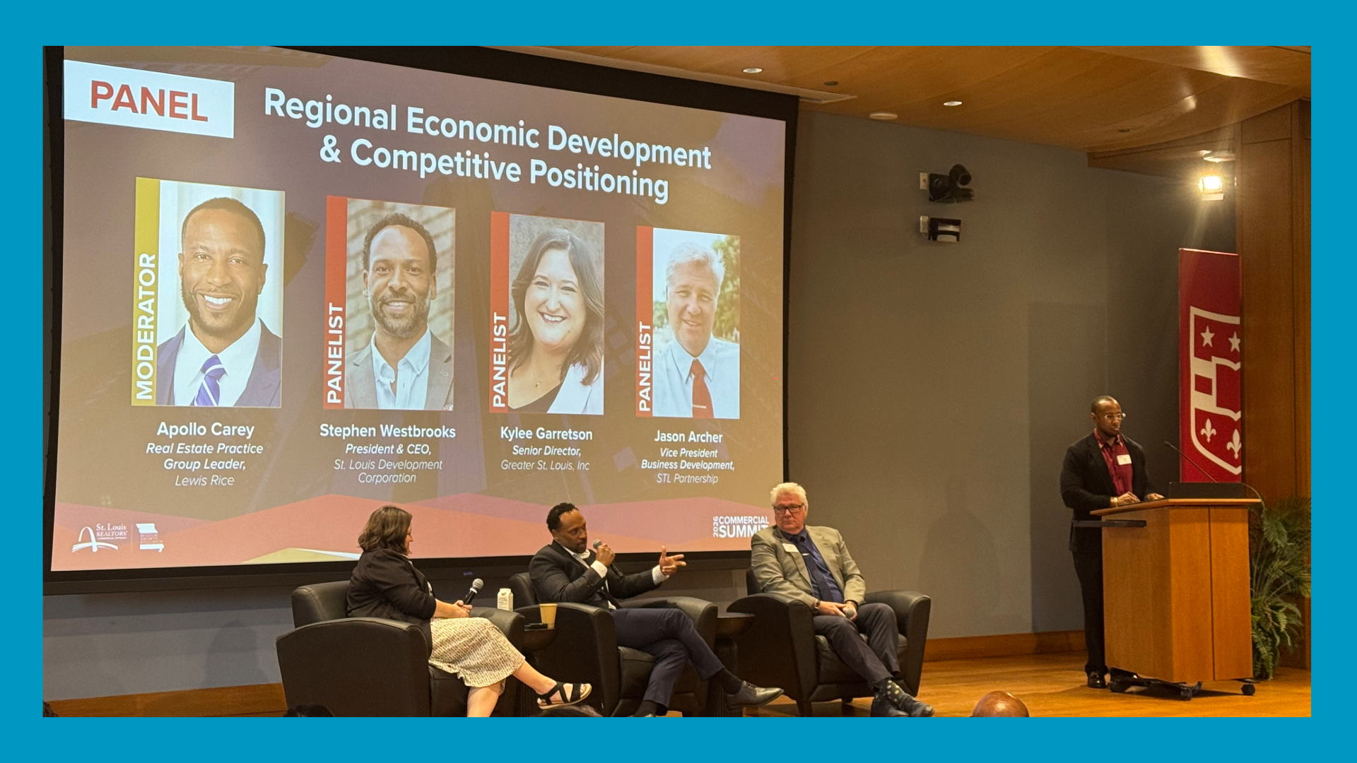 a blue border surrounds an image of 3 people sitting on a stage panel with a powerpoint behind them and someone at a podium to the right