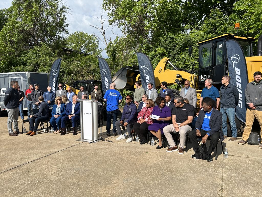 a large assortment of officials gather behind a podium, mostly sitting down