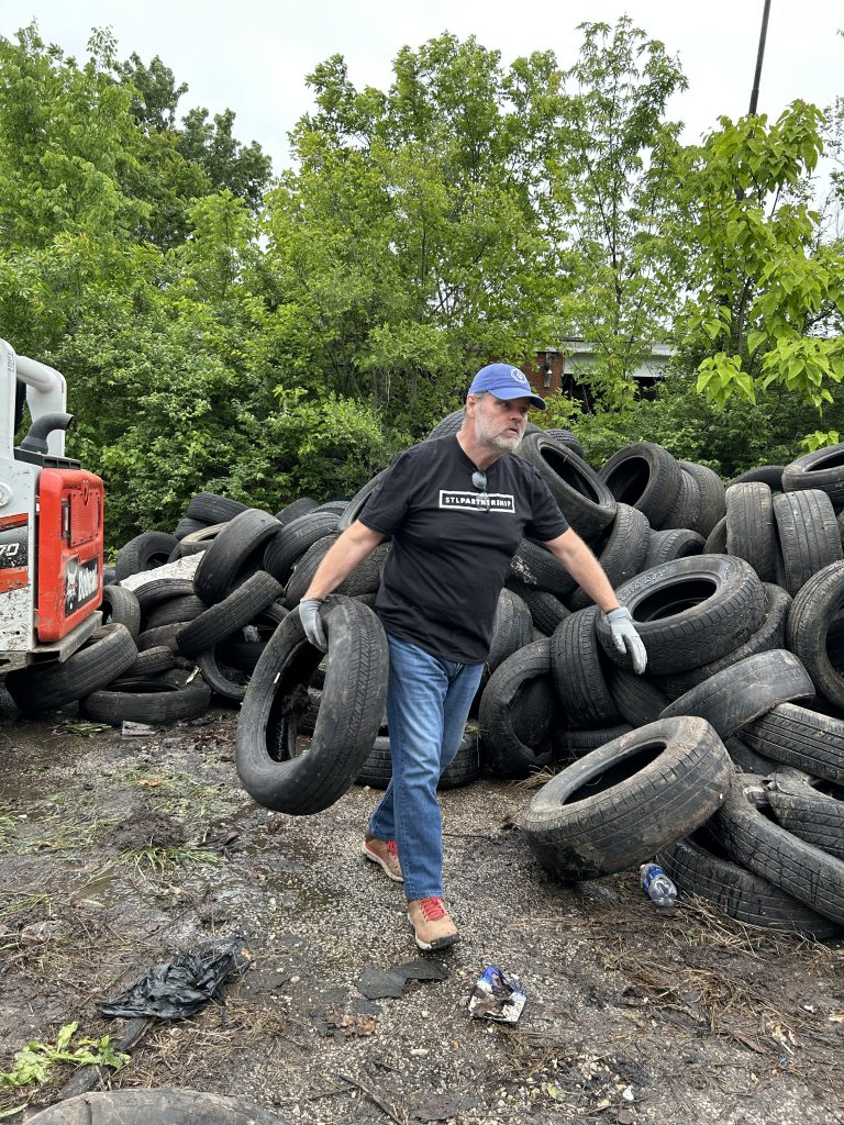 a man in a black stl partnership shirt hauls a tire from a shrinking pile of tires outside