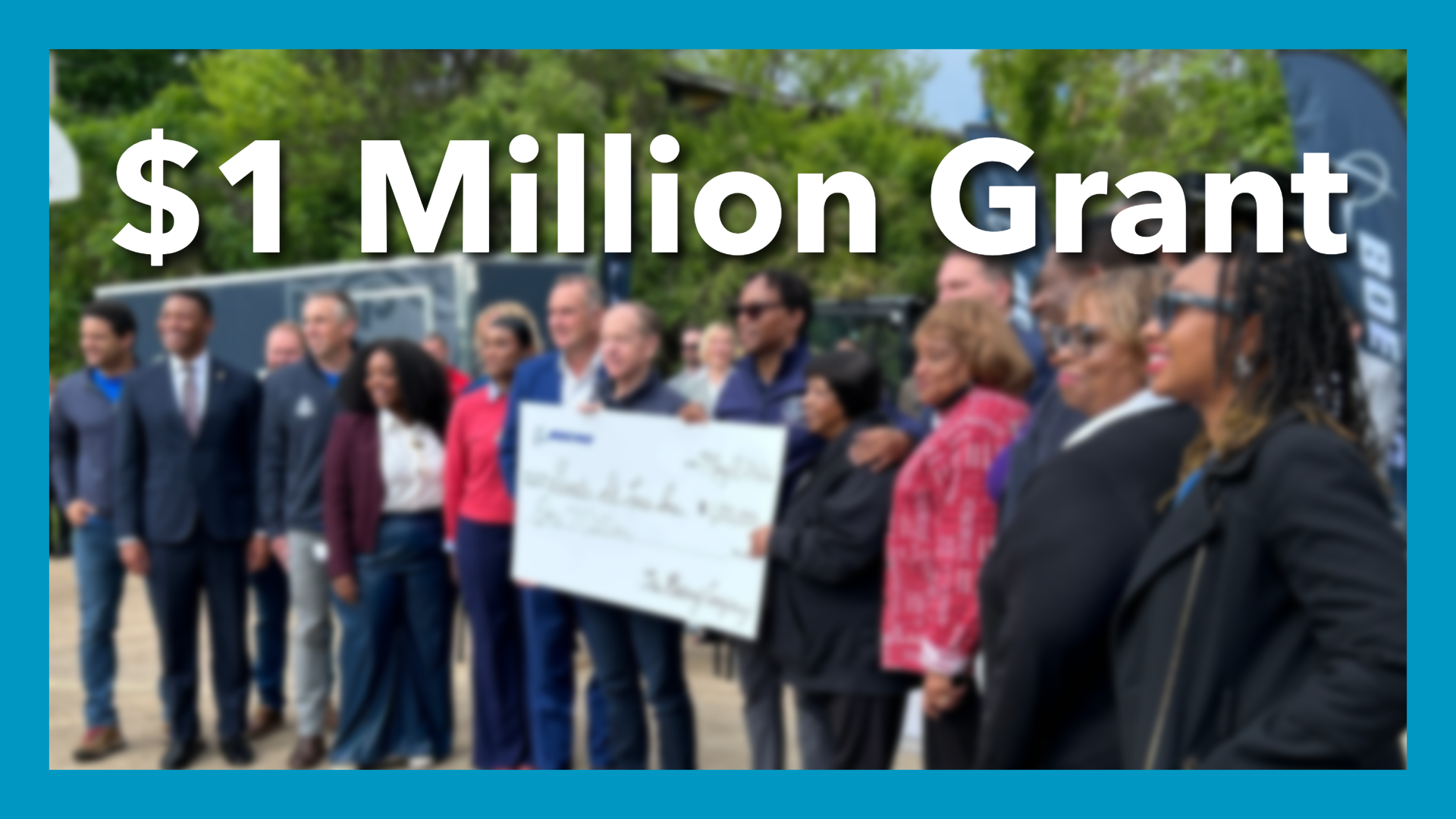 blurred photo of people holding giant check outside. The text over it reads "1 million Grant" a blue border surrounds the image