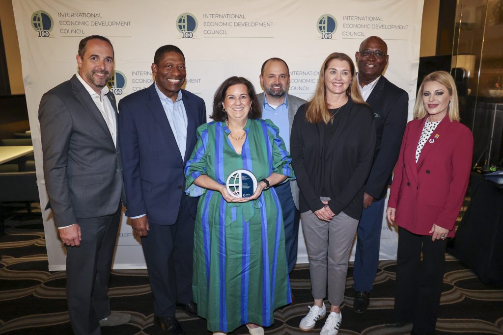 Team poses holding IEDC award in front of IEDC backdrop