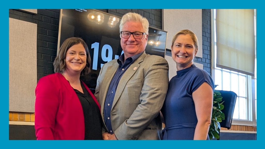 3 people stand posed for a photo - image has a blue border around it